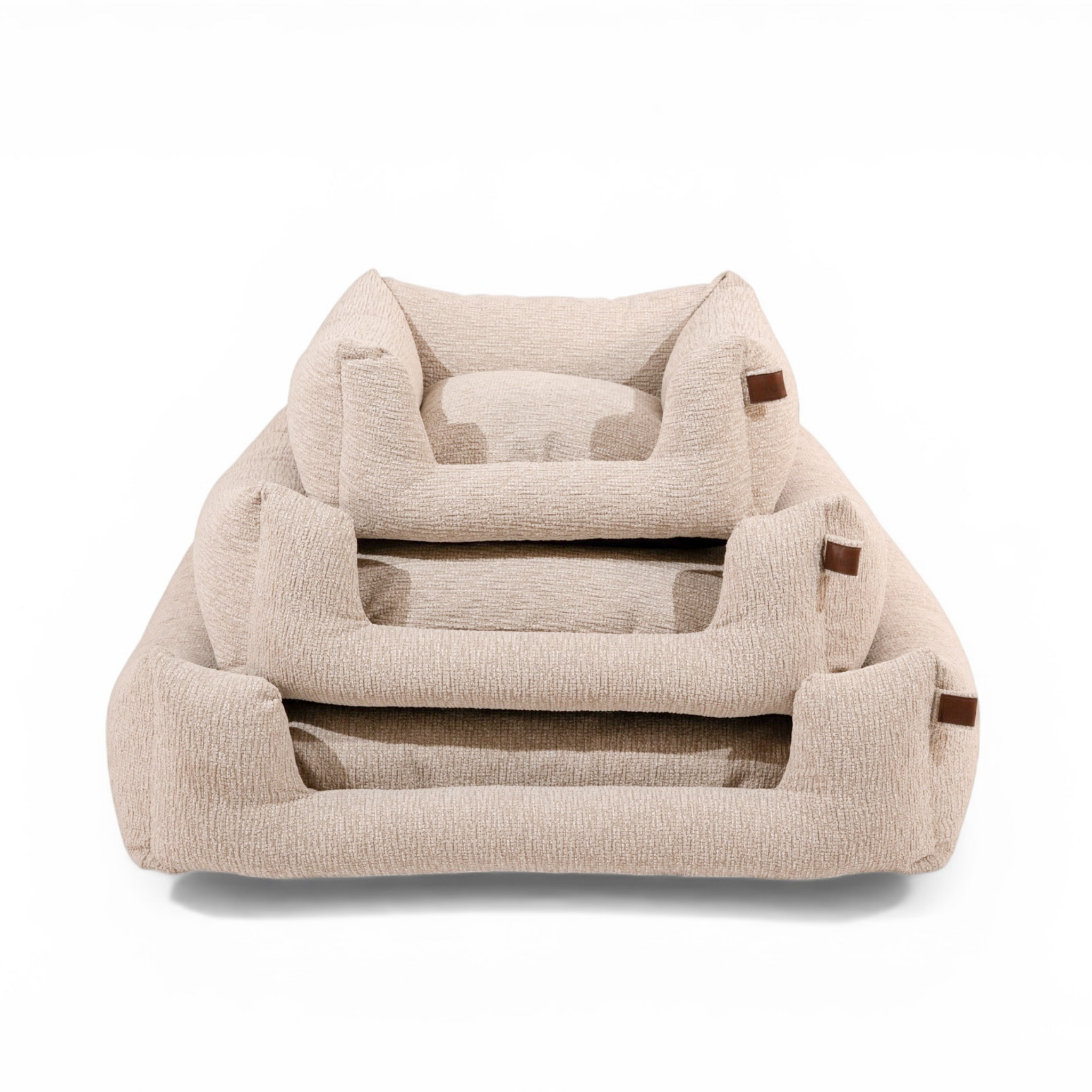 Three nested pet beds in a textured beige fabric with small brown leather accents, shown on a clean white background..