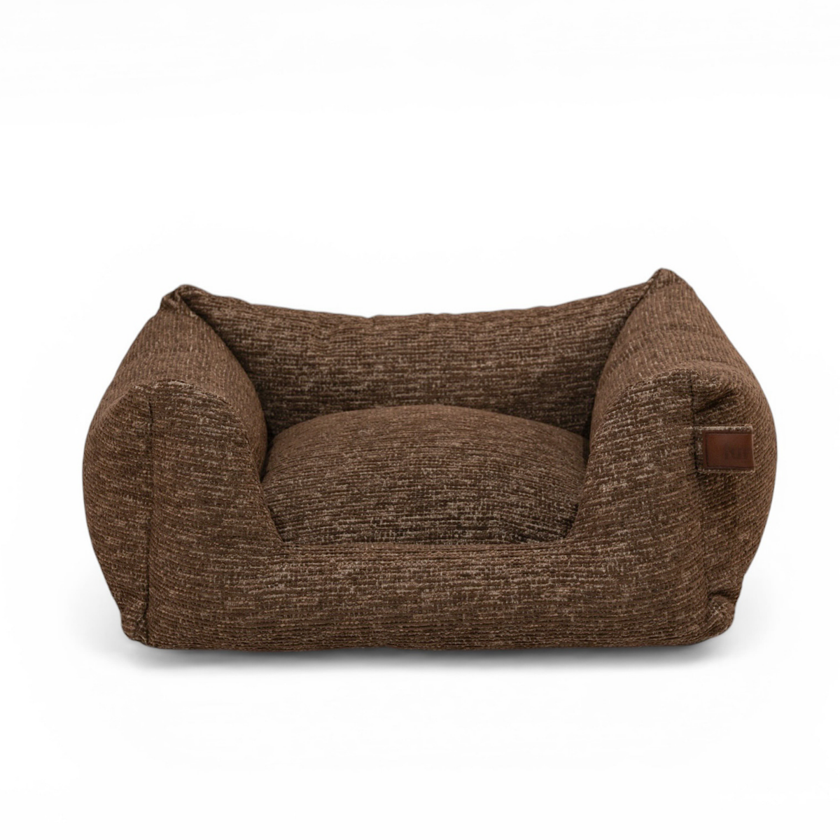A low-profile, high-cushioned pet bed upholstered in a textured brown woven fabric, featuring a small brown leather brand patch on the side, set against a plain white background.