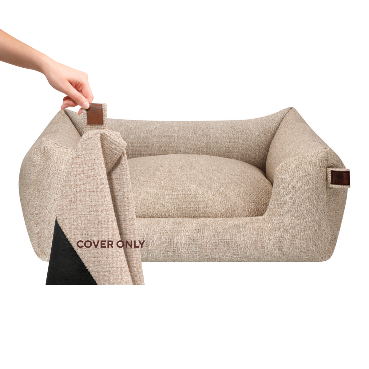Beige textured pet bed cover shown on a raised pet bed, with a hand lifting the corner to reveal the black underside. A close-up inset at the bottom left shows the fabric texture and a brown tab detail.