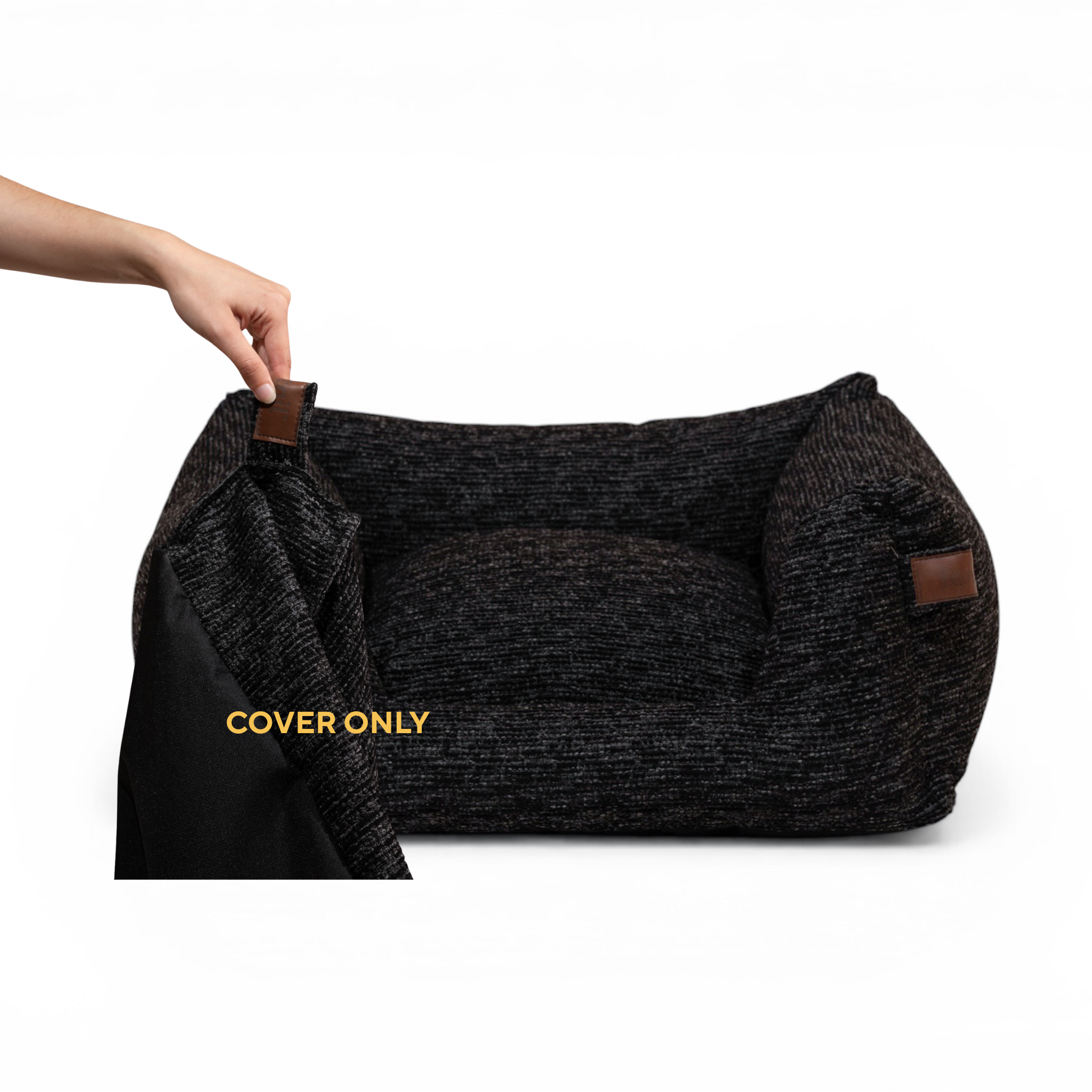 A dark charcoal textured pet bed with brown leather-like corner tabs, shown with a hand lifting a black cover. Yellow text reads 'COVER ONLY'.