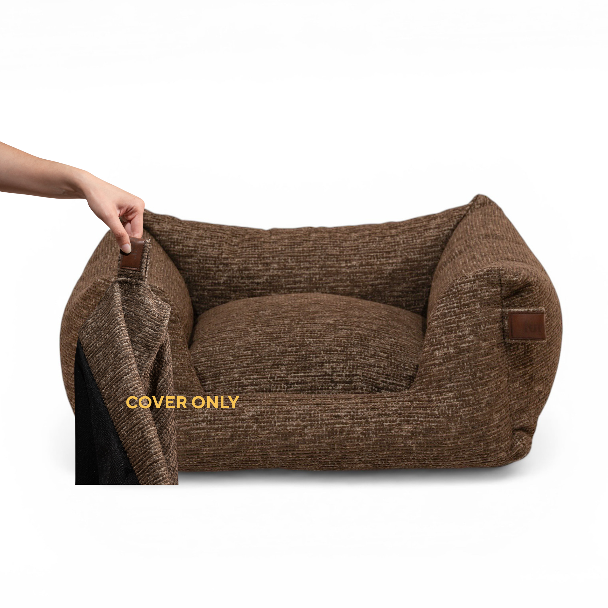 A brown textured pet bed with a matching cushion, shown on a white background. A human hand is pulling open a cover on the left side of the bed, revealing a black interior.