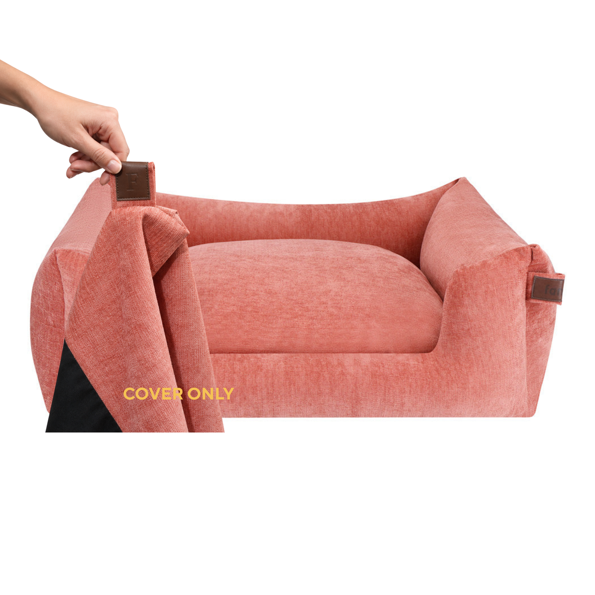 A dusty rose pink pet bed with a plush cushion and raised sides, shown on a white background. A human hand is pulling up the left side of the cover, revealing a black underside and a small brown tab.