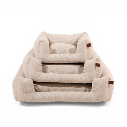 Three nested pet beds in a textured beige fabric with small brown leather accents, shown on a clean white background..