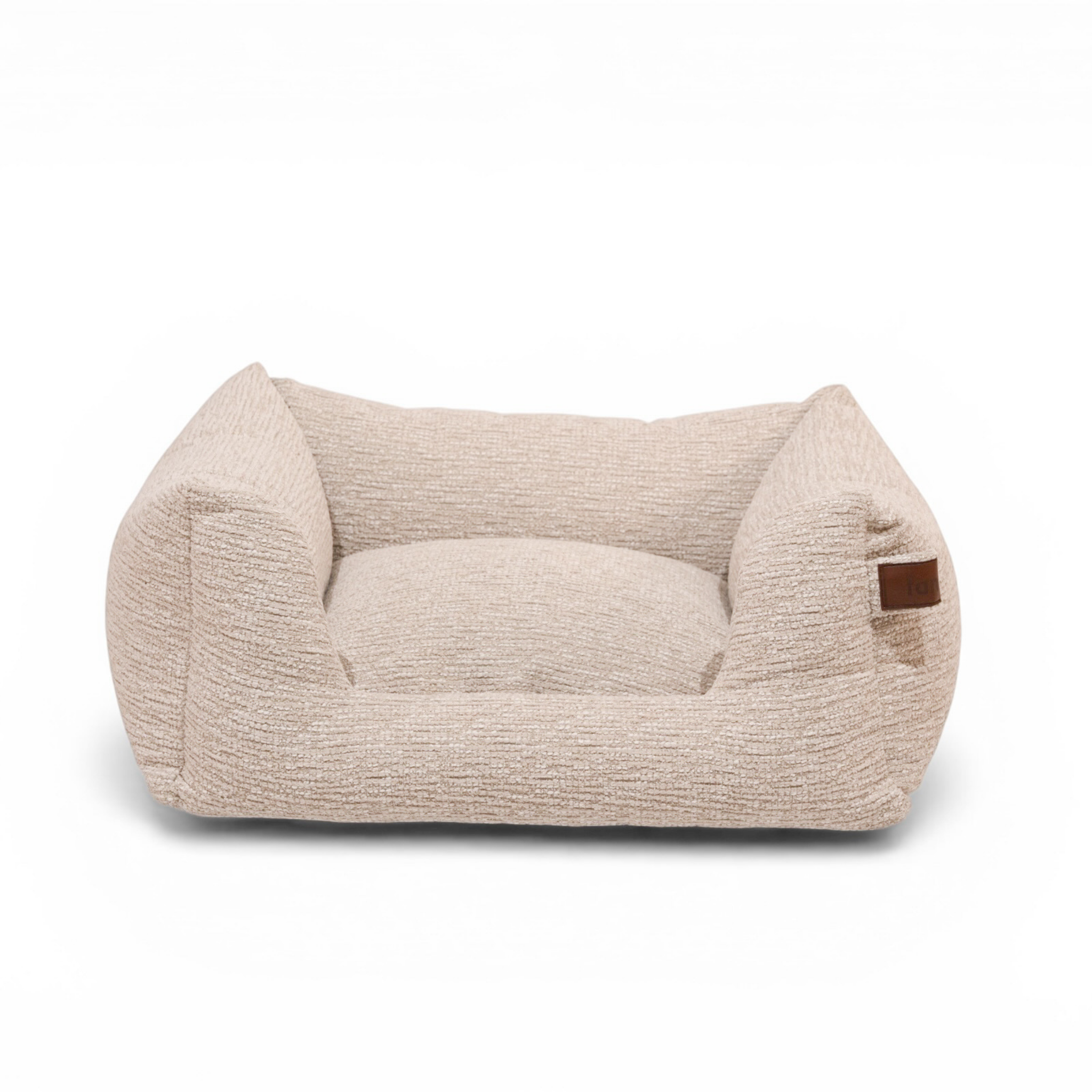 A low-profile rectangular pet bed with a textured, bouclé-like fabric in a light beige color, featuring a small brown leather brand patch on the right armrest, set against a plain white background.#color_clay-beige