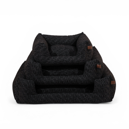 A dark charcoal gray heathered pet bed with small brown leather accents, shown on a clean white background.