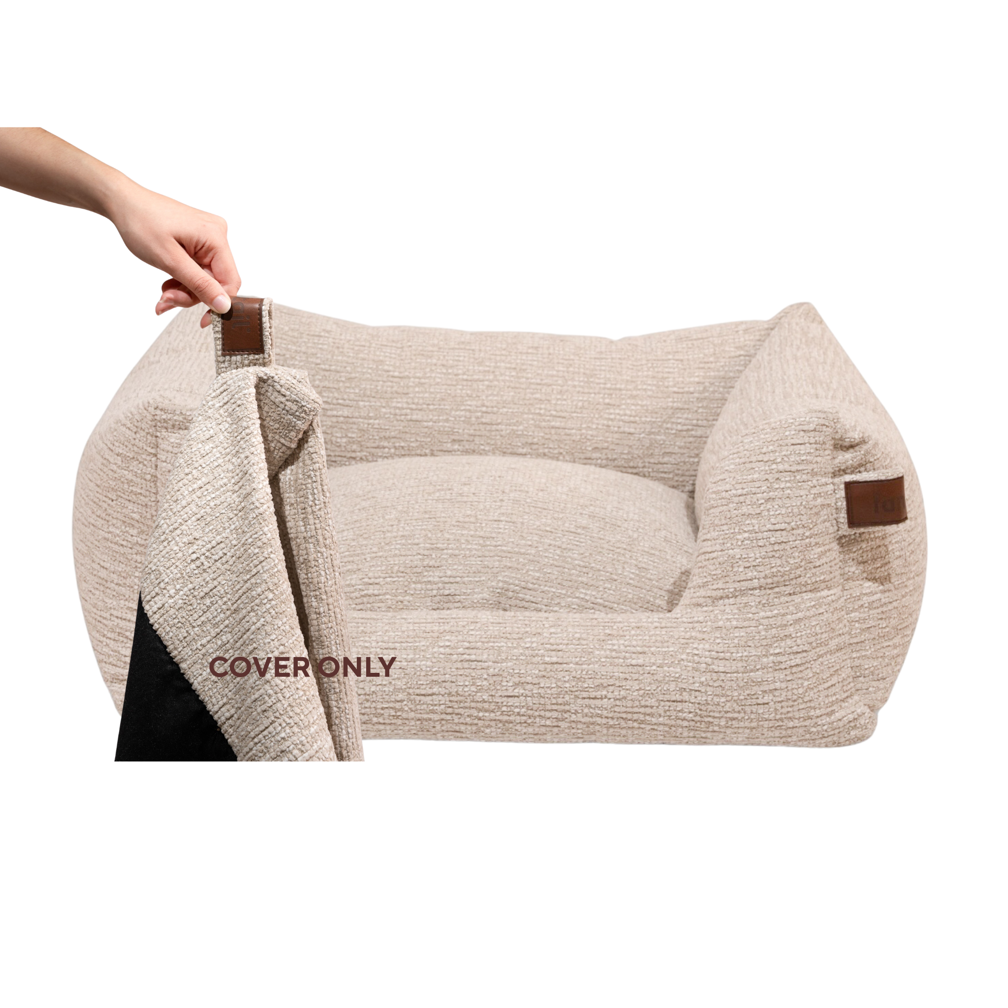 A beige textured pet bed with brown leather-like corner accents, shown on a white background with a hand lifting the cover to reveal a black interior.#color_clay-beige
