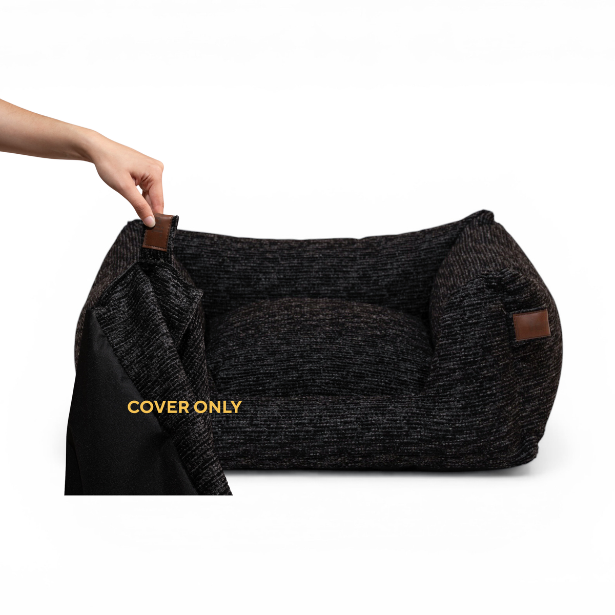 A dark charcoal textured pet bed with brown leather-like corner tabs, shown with a hand lifting a black cover. Yellow text reads 'COVER ONLY'. 