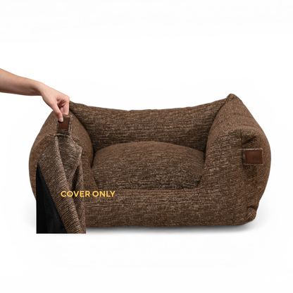 A brown textured pet bed with a matching cushion, shown on a white background. A human hand is pulling open a cover on the left side of the bed, revealing a black interior. 